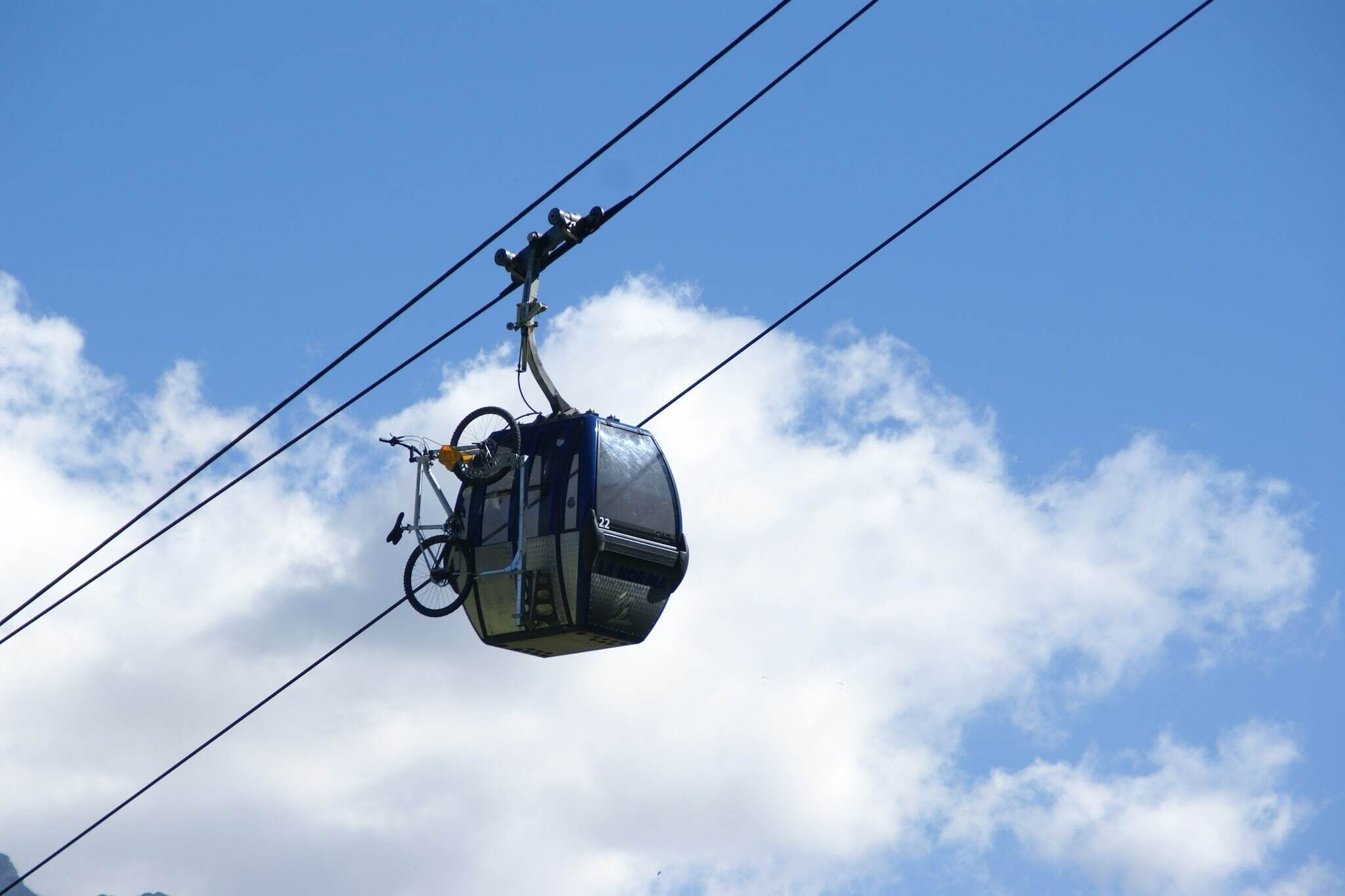 A cable car suspended between two towers, with a clear sky and clouds in the background.