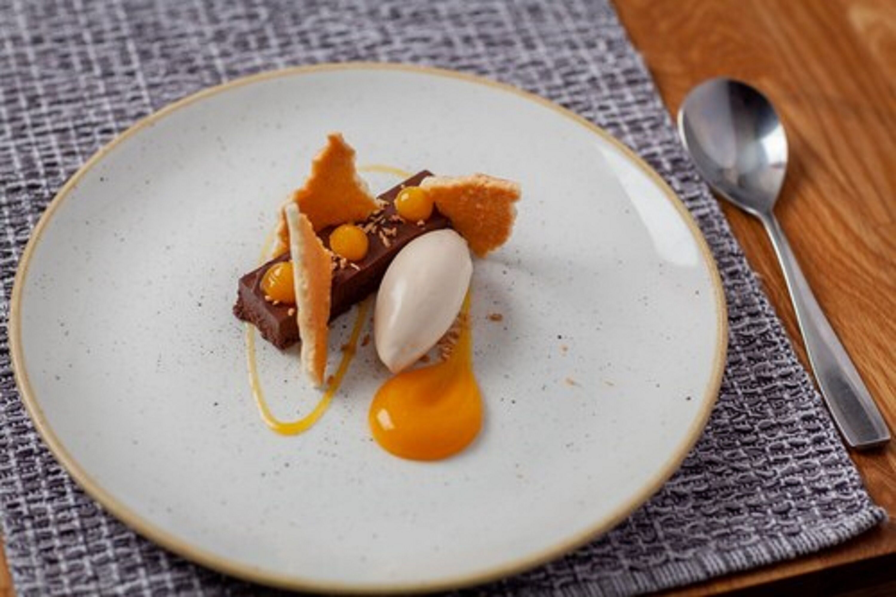 A dessert on a plate with a spoon and a knife on a textured tablecloth.