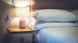 A neatly made bed with white linens and a wooden nightstand with a lamp. - The Seaview Hotel (Seaview)