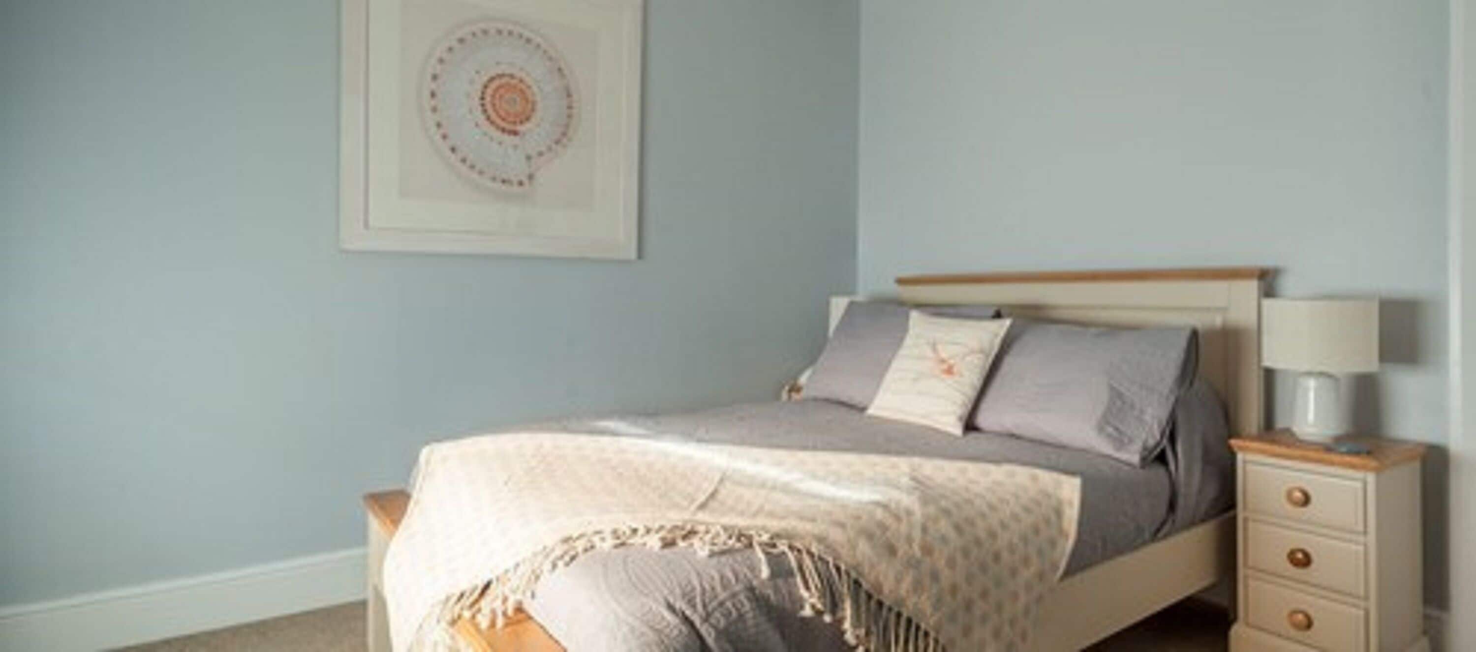 Un dormitorio con una cama, una mesita de noche, una lámpara y un cuadro colgado en la pared.