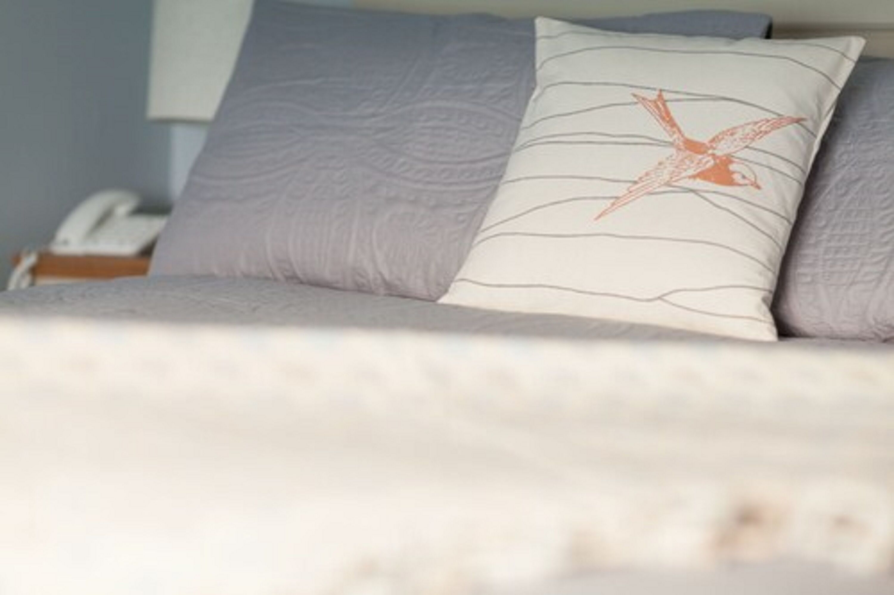 A bed with a grey bedspread and pillows, one with a bird design.