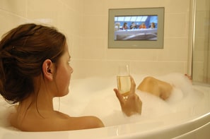 A person relaxing in a bathtub with a television mounted on the wall. - The Seaview Hotel (Seaview)