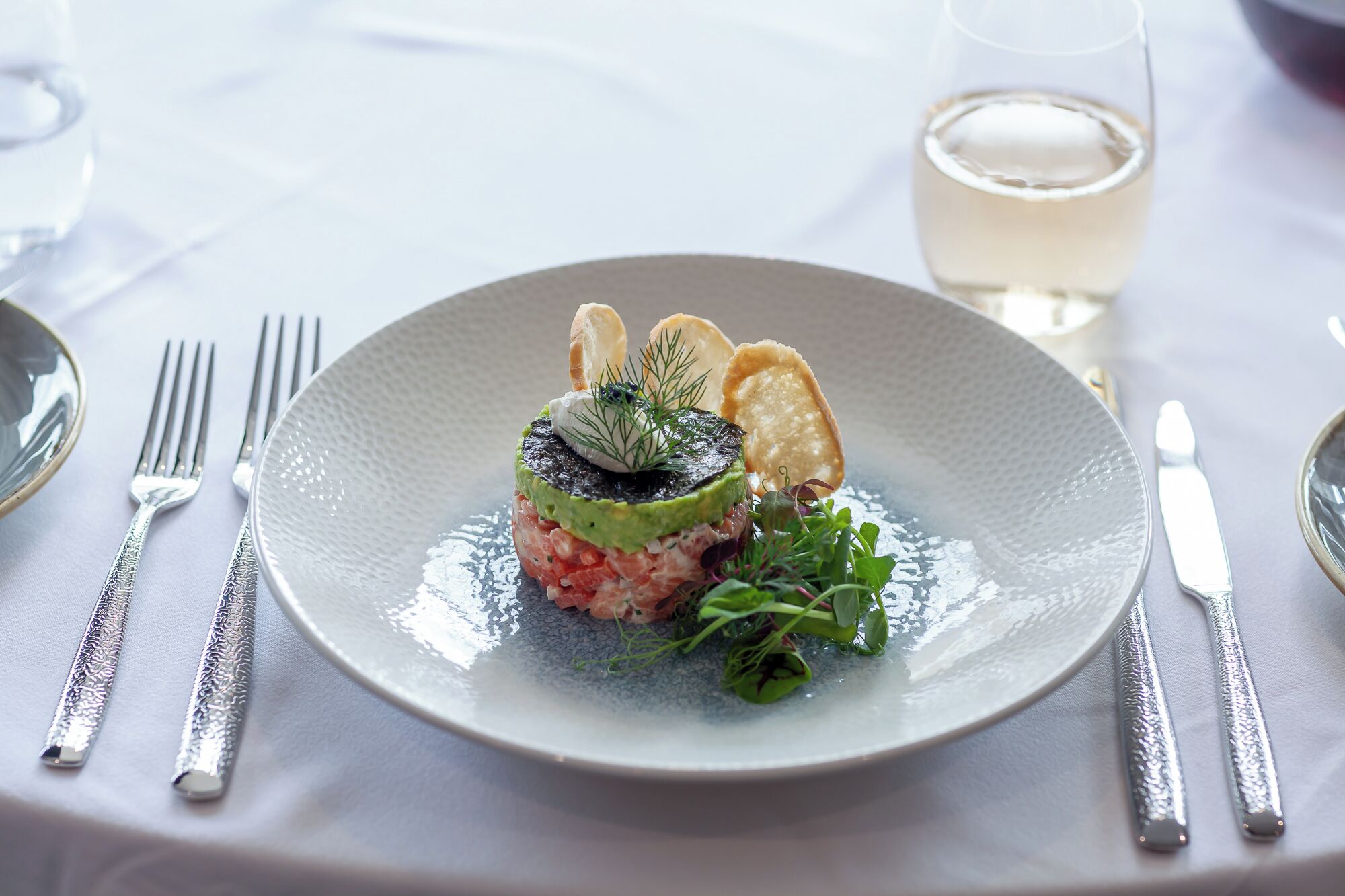 A plated dish with a glass of white wine on a table.