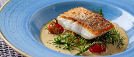 Ein Teller mit Fisch, Kirschtomaten und Kräutern.