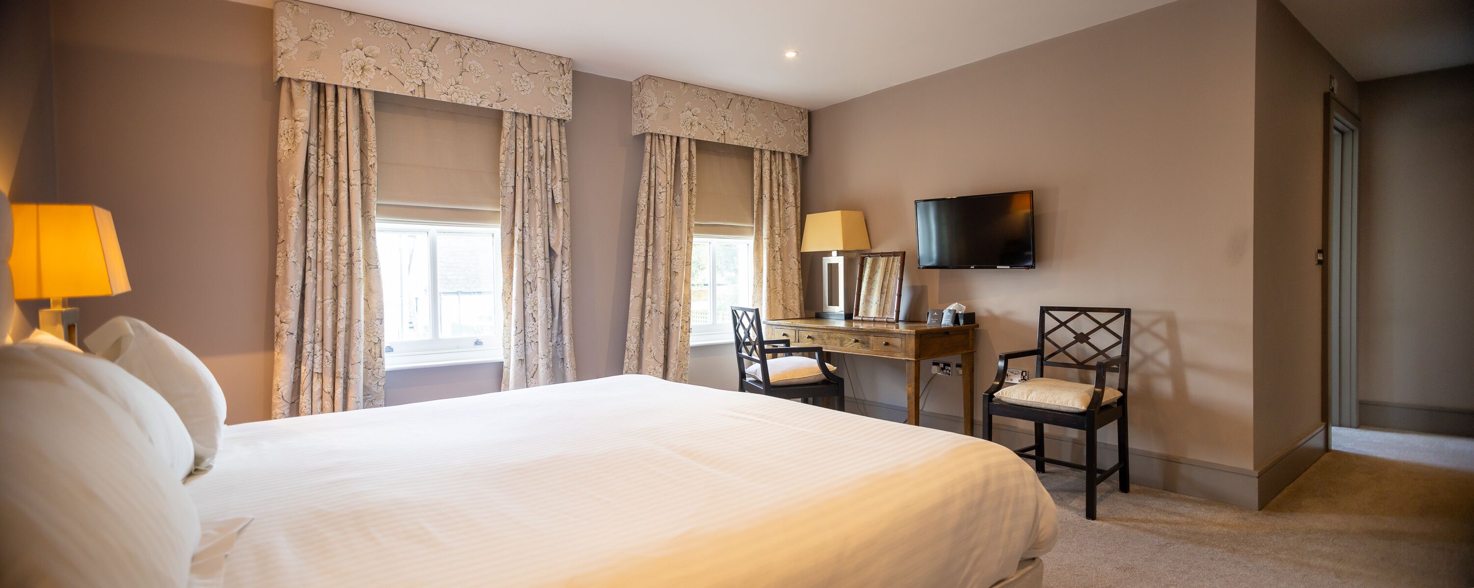 A hotel room with a large bed, a desk with a chair, a television, and curtains.