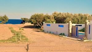 A coastal property with a dirt path leading to a gated entrance, surrounded by olive trees and a view of the sea. - Charming Beach House with private pool in South Rhodes, Beach Pearl (Gennadi)
