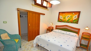 A bedroom with a bed, a chair, a nightstand, a painting, and a door. - Luxury villa with large terrace overlooking the sea and a few steps from the sea (Marina San Gregorio)