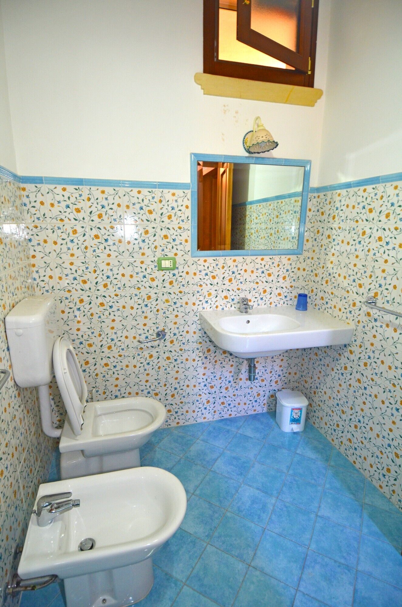 Ein Badezimmer mit Toilette, Bidet und Waschbecken, mit Blumenmuster gefliest.