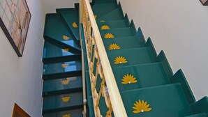 A staircase with green steps and yellow flower decorations, a wooden handrail, and a window with a view of a building. - Luxury villa with large terrace overlooking the sea and a few steps from the sea (Marina San Gregorio)