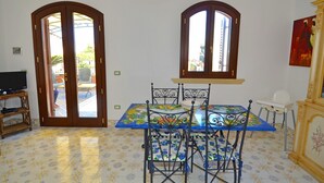 A dining area with a table and chairs, a television, and an air conditioning unit. - Luxury villa with large terrace overlooking the sea and a few steps from the sea (Marina San Gregorio)