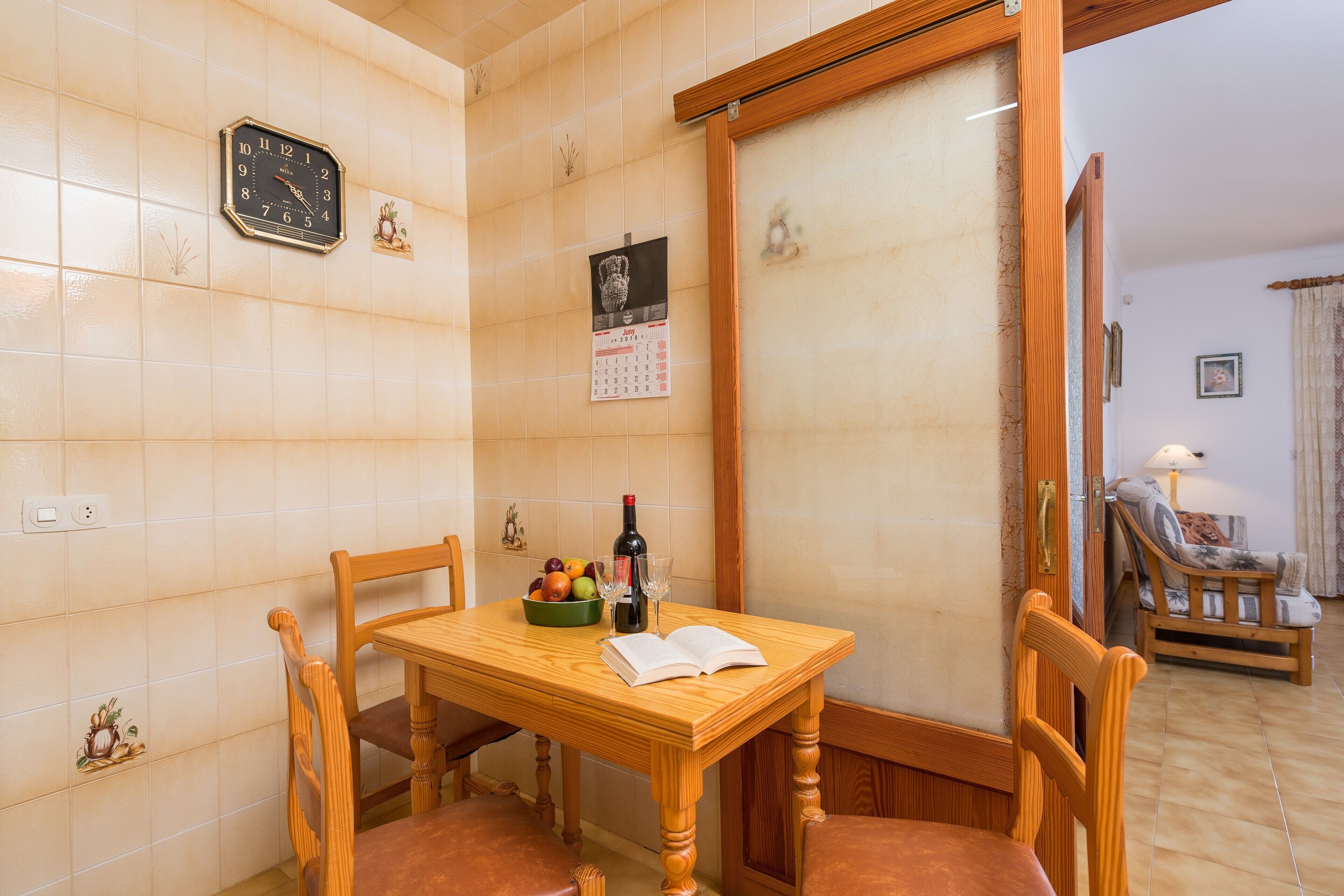 Un coin repas avec une table en bois, des chaises, une horloge, un calendrier et une bouteille de vin.