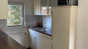 Eine kleine Küche mit weißen Schränken, einer Mikrowelle, einem Spülbecken und einem Fenster.