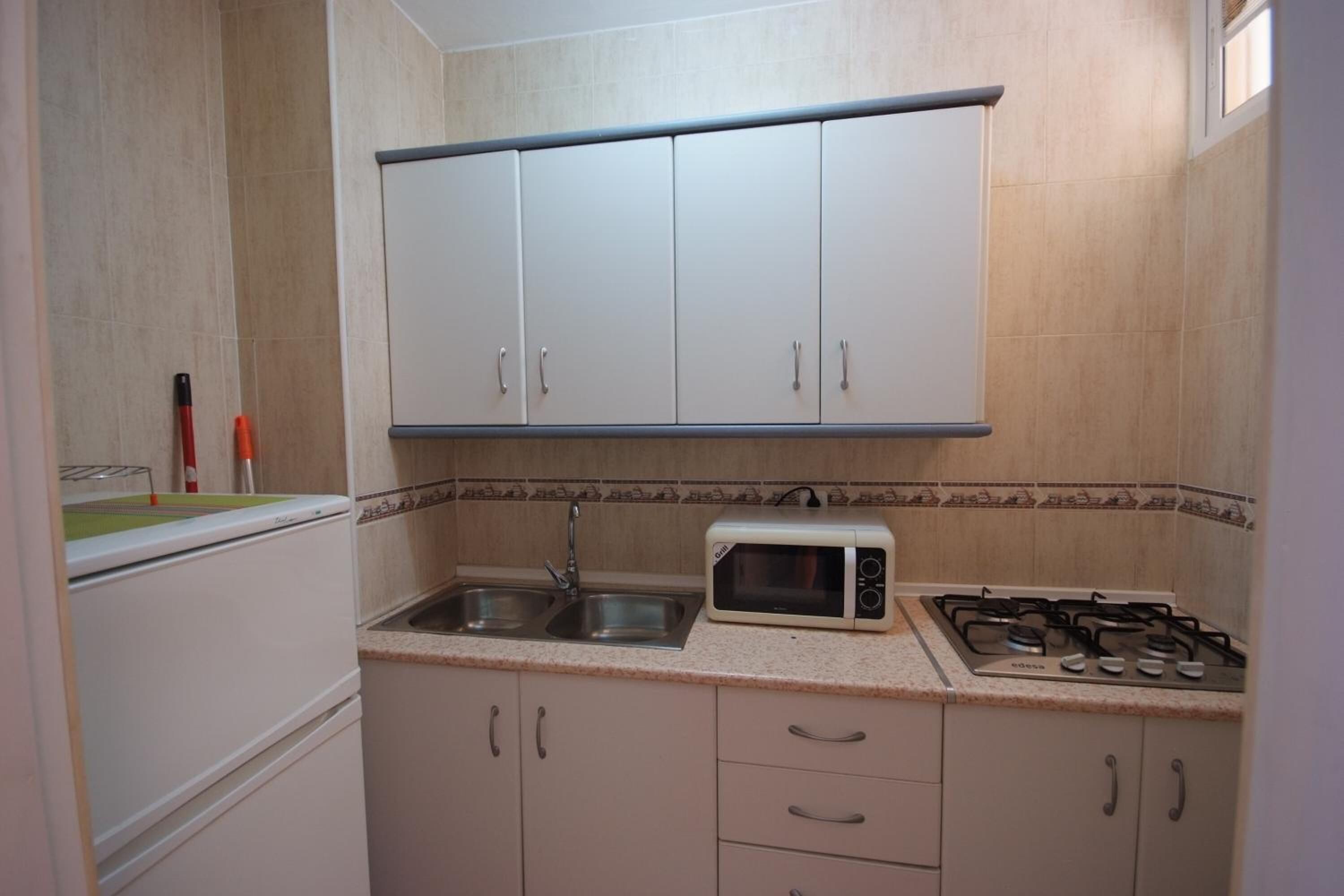 A compact kitchen with white cabinets, a microwave, a gas stove, and a sink.