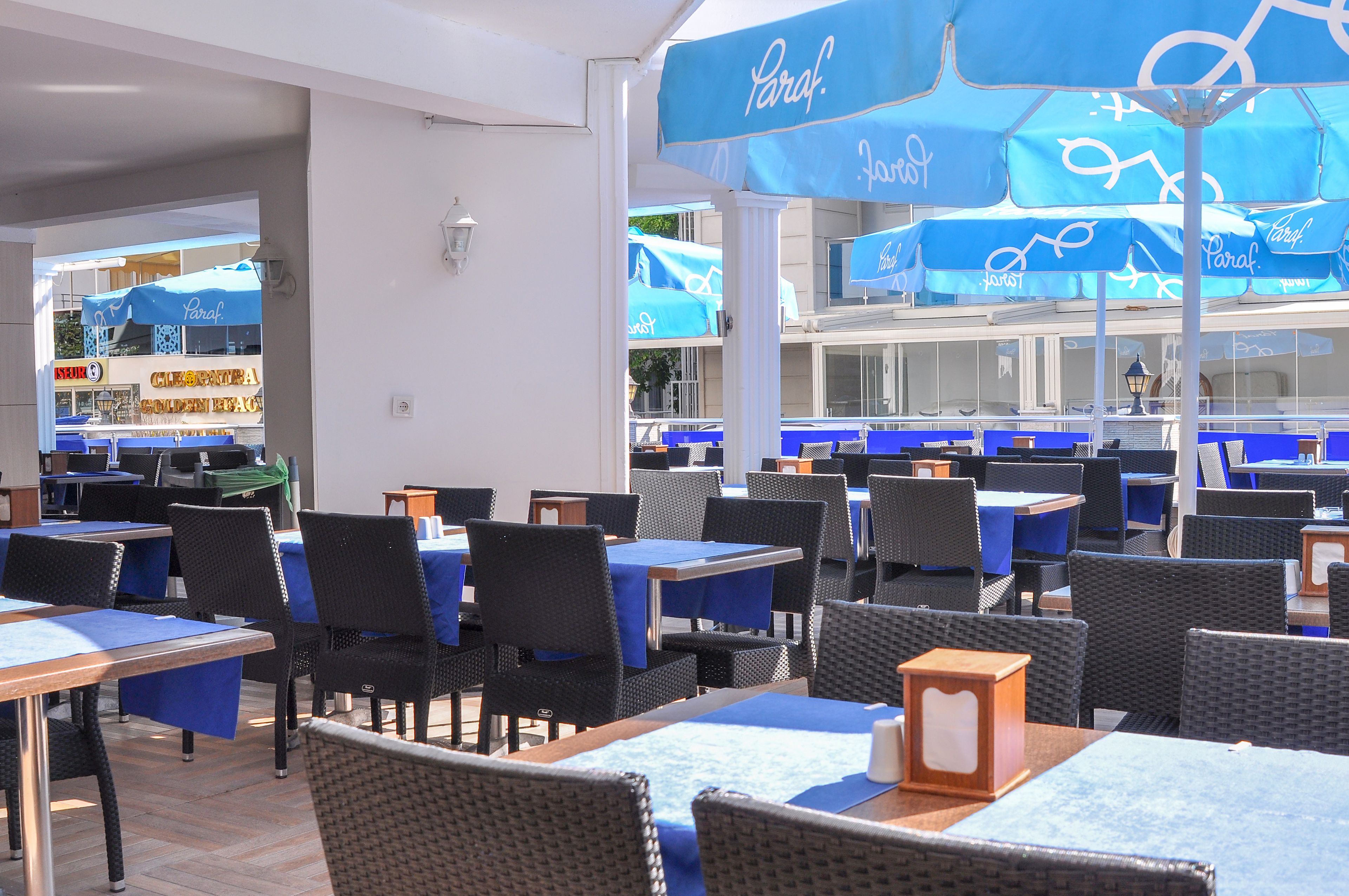 A restaurant with blue tables and chairs, and umbrellas with the word "Paraf" on them.