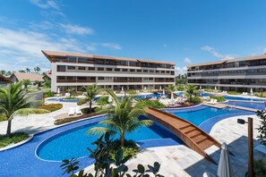 Een resort met een groot zwembad, meerdere balkons en palmbomen.