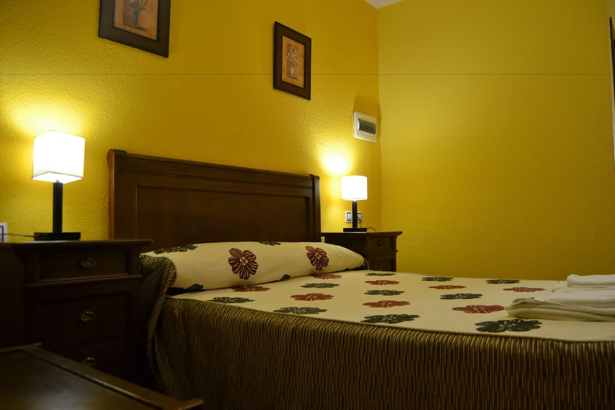 A hotel room with a bed, two bedside lamps, a nightstand, and a wooden headboard.