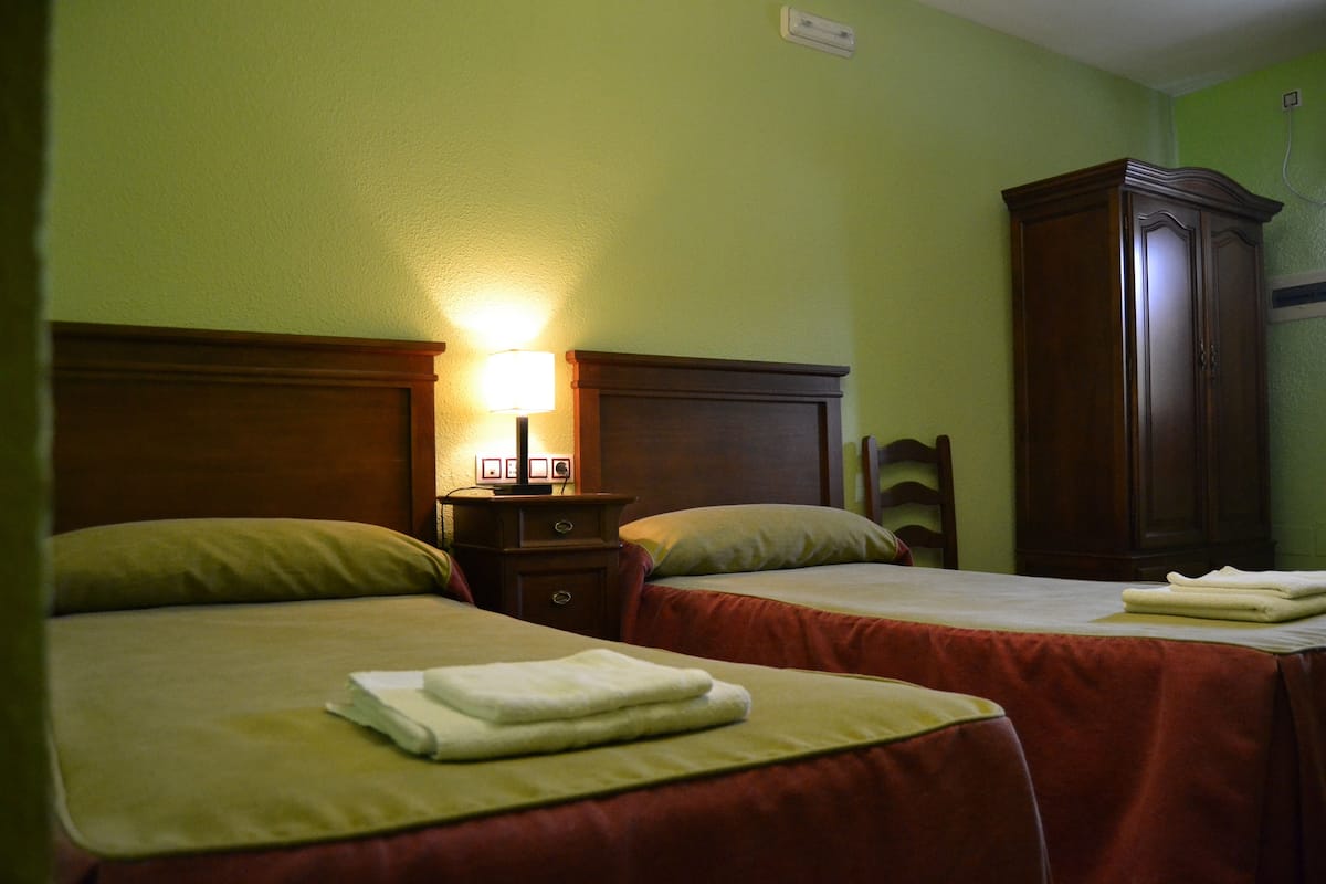 A hotel room with two beds, a nightstand with a lamp, and a wooden wardrobe.