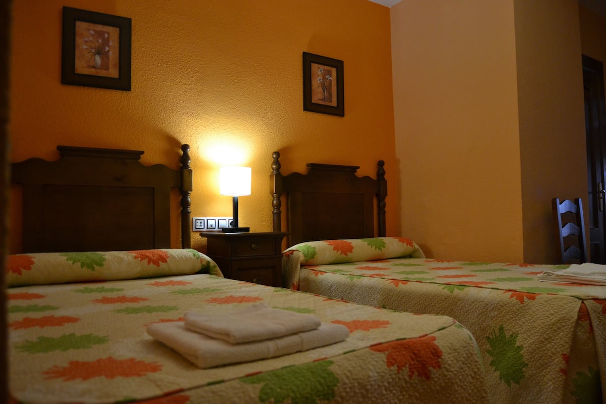 A hotel room with two beds, a nightstand, a lamp, and framed artwork on the walls.