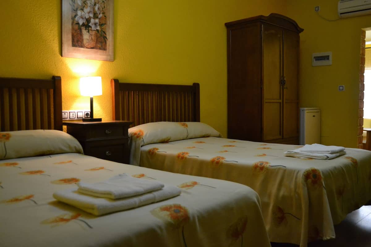 A hotel room with two beds, a nightstand with a lamp, a wardrobe, and an air conditioning unit.