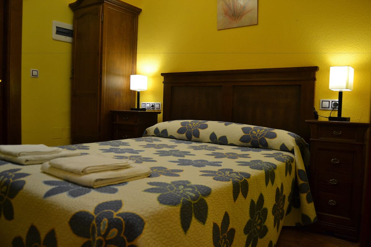 A hotel room with a bed, two bedside tables with lamps, a wooden wardrobe, and a yellow wall.