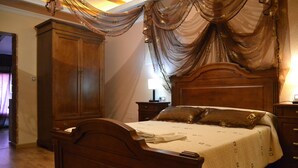 Una cama con dosel de madera, con una colcha blanca y dos almohadas, flanqueada por mesitas de noche de madera y un amplio armario.