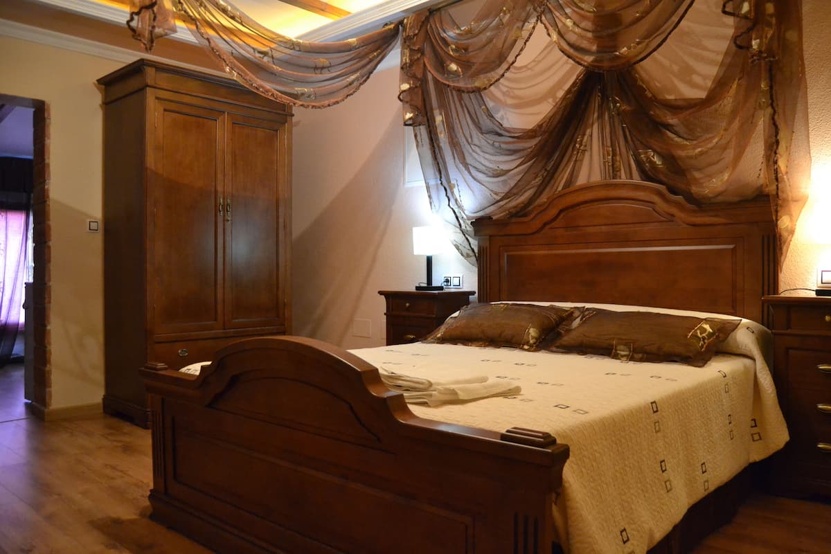 A wooden four-poster bed with a white bedspread and two pillows, flanked by wooden nightstands and a large wardrobe.