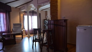 Una sala de estar con piso de madera, un refrigerador blanco, un armario de madera, una silla y una mesa.
