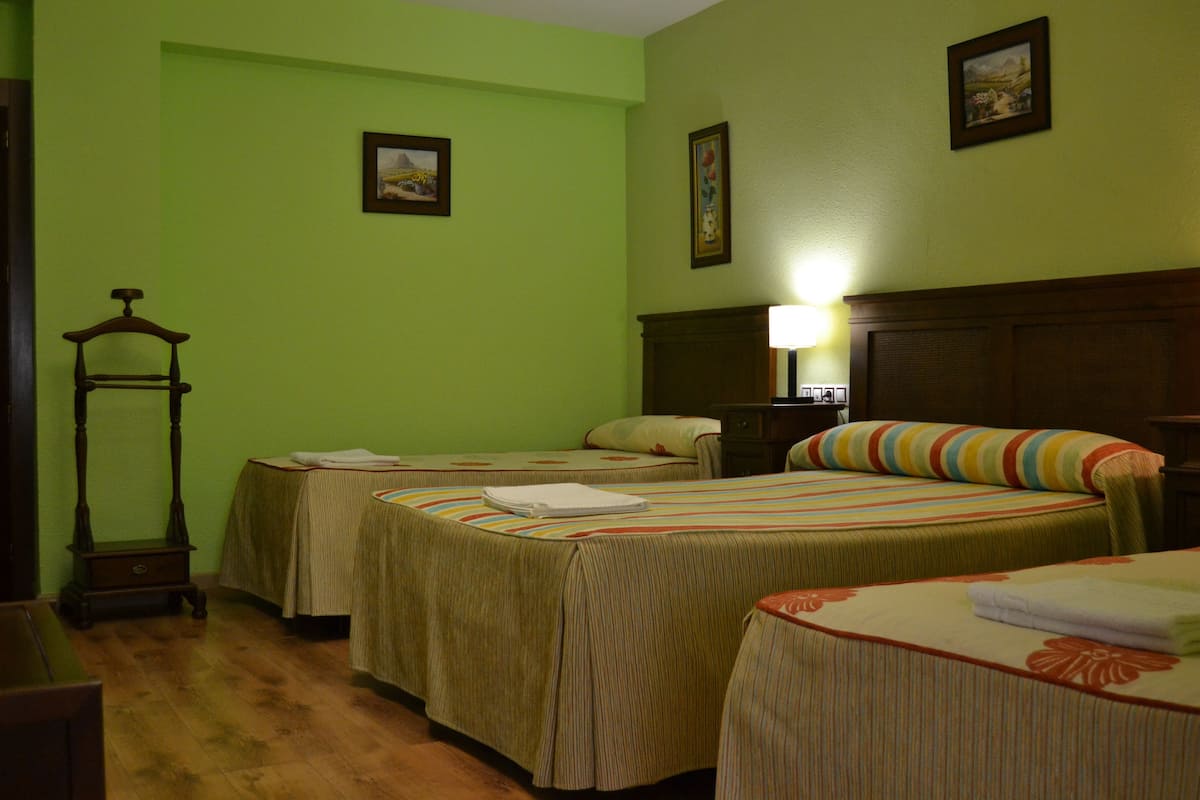 A room with two beds, a wooden nightstand, a lamp, and a small table.