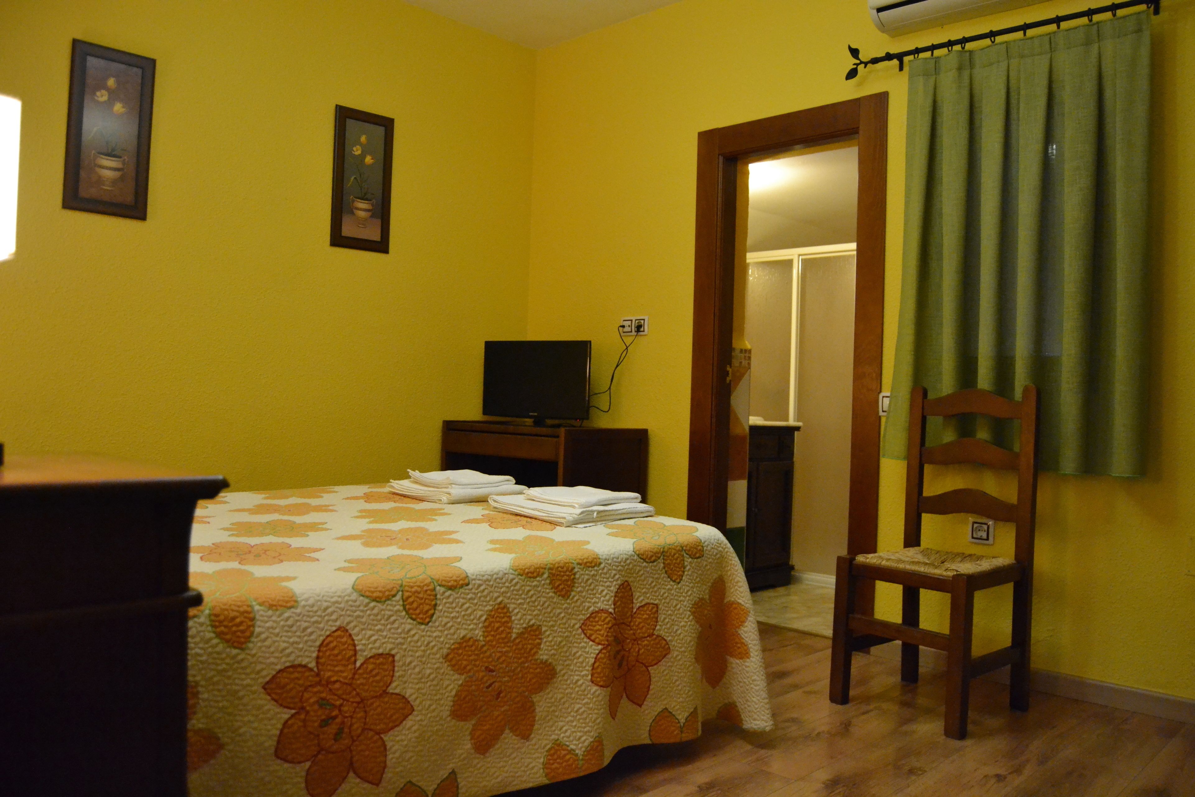A room with a bed, a chair, a television, and a door leading to another room.
