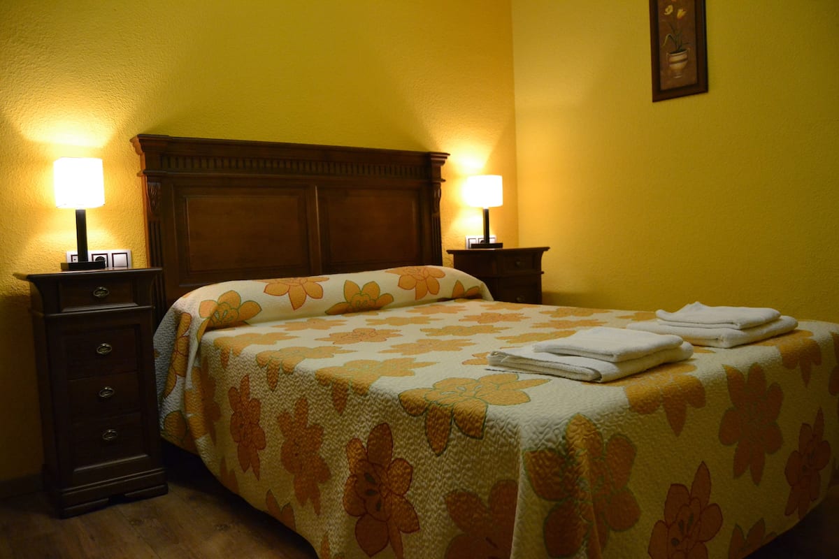 A hotel room with a floral bedspread, two bedside lamps, and a wooden headboard.