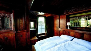 A wooden room with a bed, a window with curtains, and a mirror. - De Zwerver (Naarden)