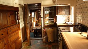 A narrow kitchen with wooden cabinets, a tiled floor, and a window with a view of the outside. - De Zwerver (Naarden)