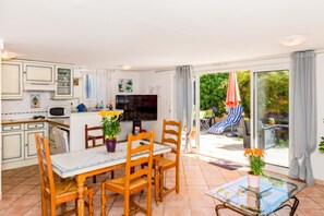 Una cocina moderna con comedor, televisor y vista al jardín a través de puertas correderas.