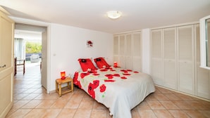A bedroom with a bed, a bedside table, a nightstand, a window, and a door leading to a balcony.