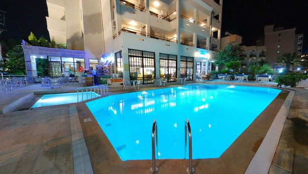Piscina com superfície de água azul cristalina, rodeada por espreguiçadeiras e um edifício com vários andares e varandas.