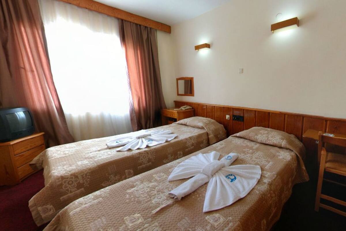 A hotel room with two beds, a wooden wardrobe, a desk with a telephone, and a television.