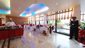 Lobby de hotel com buffet, piso de mármore e grandes janelas que oferecem vista para o exterior.