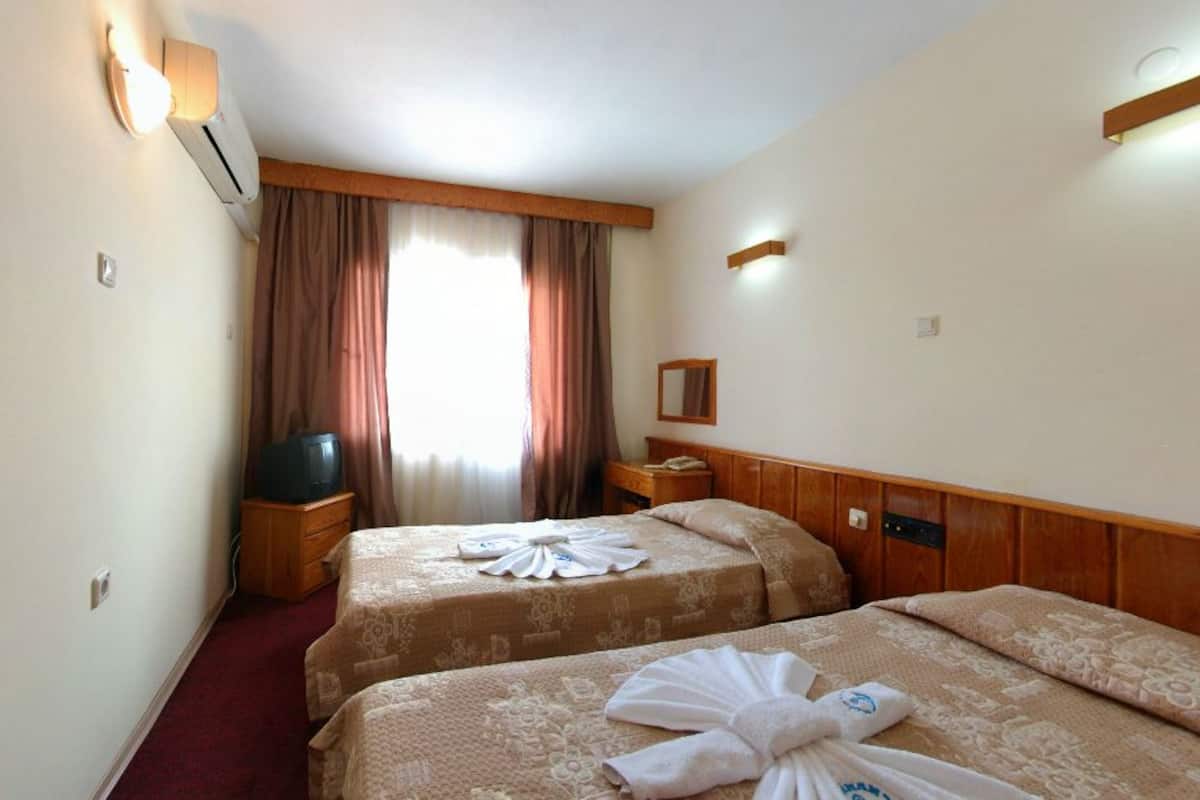 A hotel room with two beds, a television, a mirror, and a window with curtains.