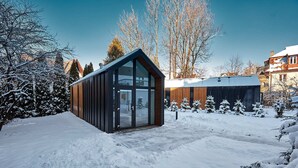 Une cabane moderne en bois, dotée de grandes portes vitrées, entourée d’arbres couverts de neige et surplombant un ciel dégagé.