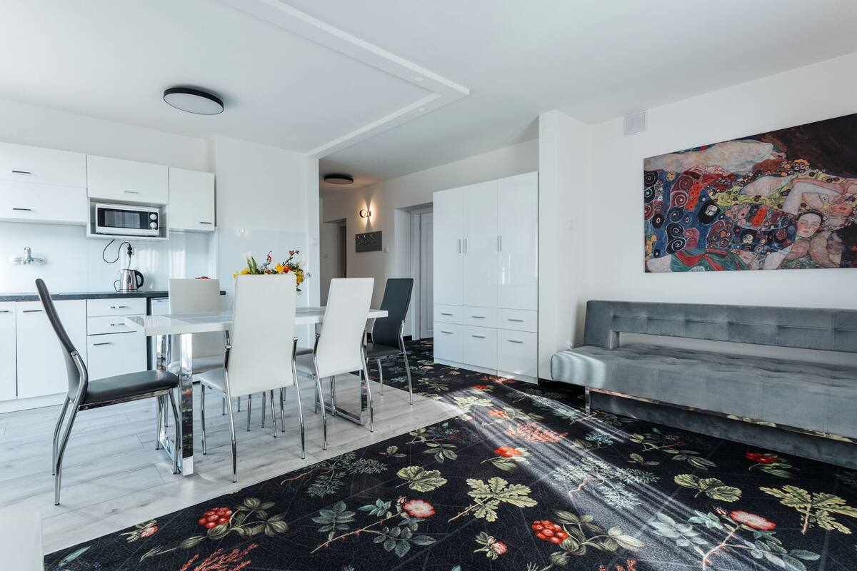 Una cocina moderna con armarios blancos, un comedor con mesa y sillas, y un cuadro abstracto grande en la pared.