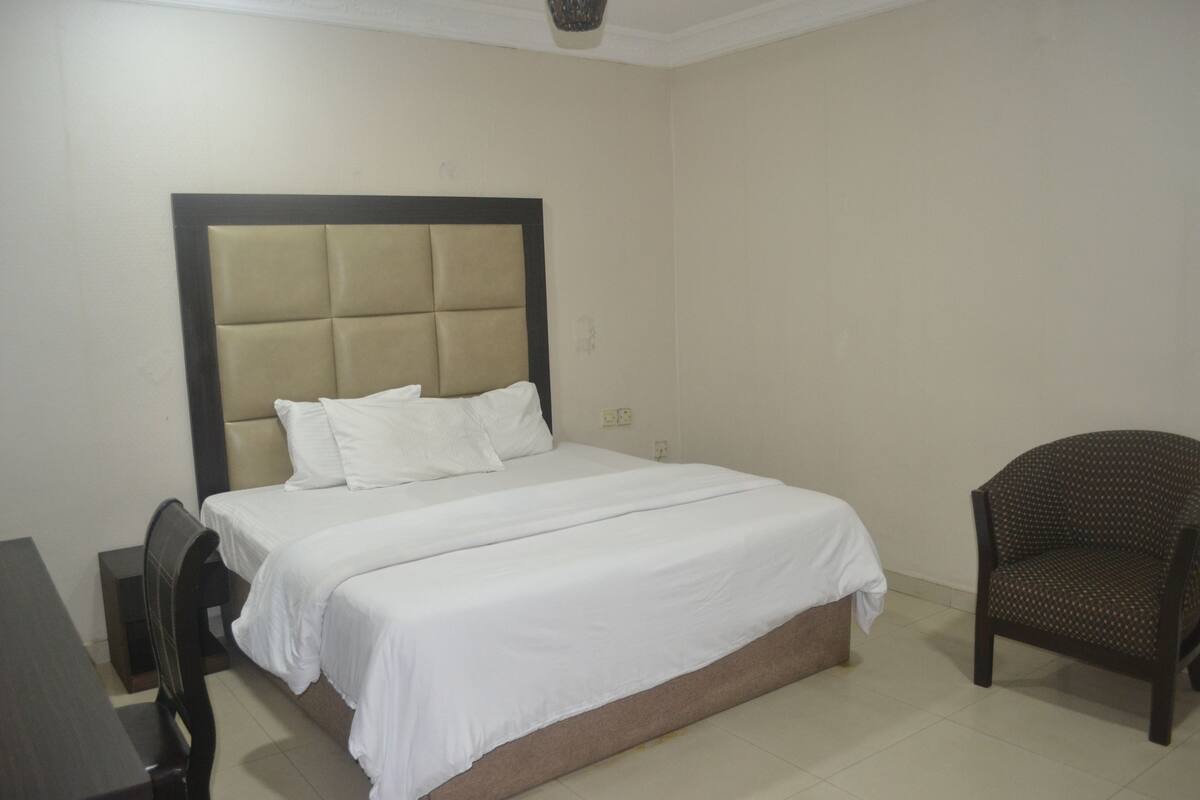 Un dormitorio ordenado con una cama grande, una silla y una mesita.