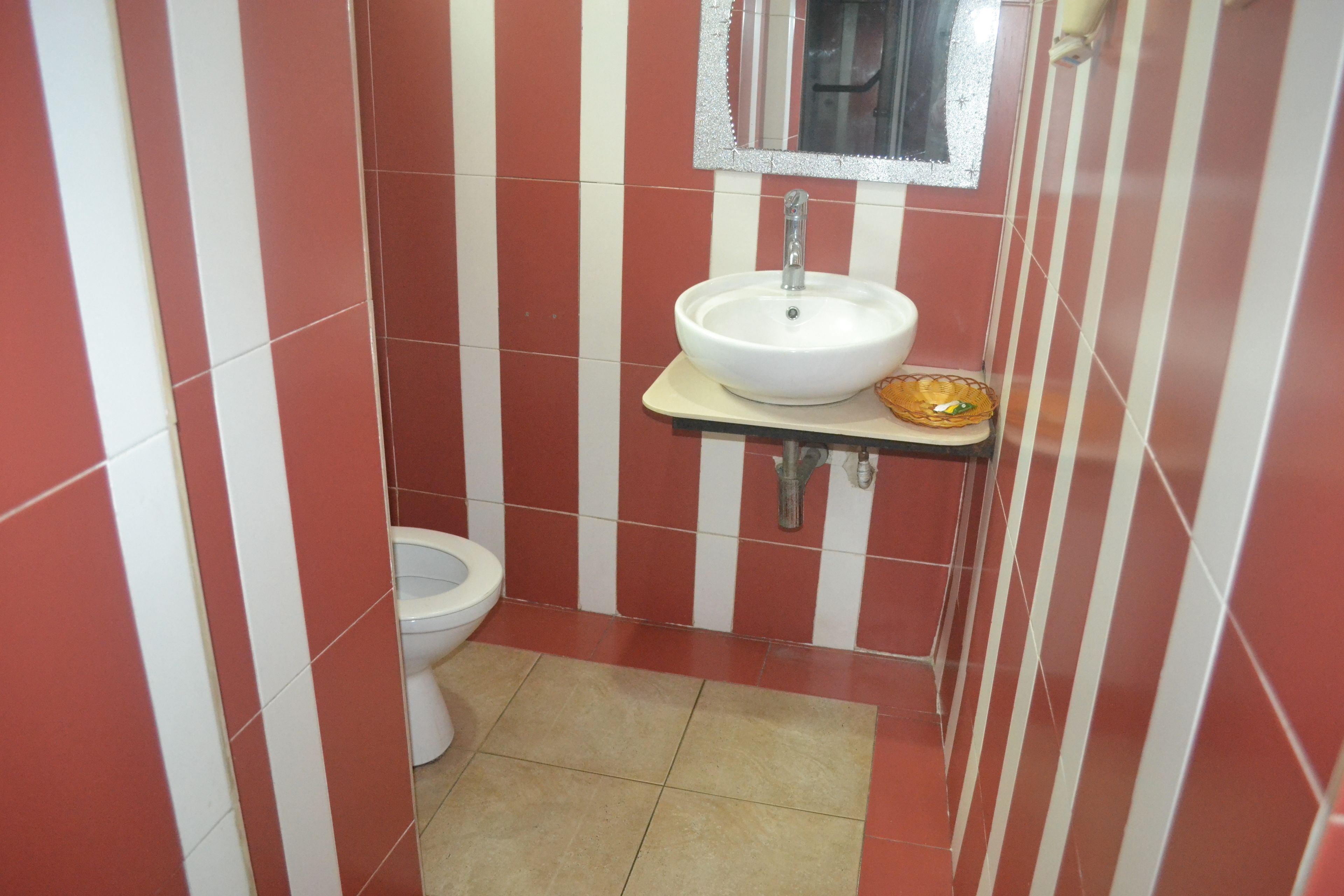 Un baño pequeño con paredes a rayas rojas y blancas, un lavamanos blanco y un inodoro.