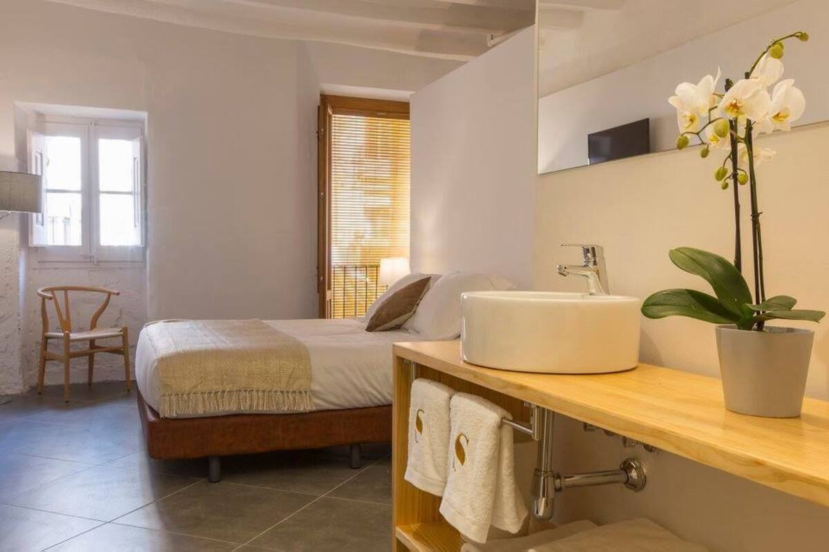 A bedroom with a bed, a bedside table with a sink, a chair, and a potted orchid.