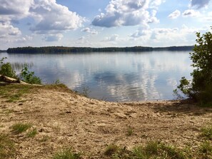 A calm lake with a sandy shore and a forested island in the distance.