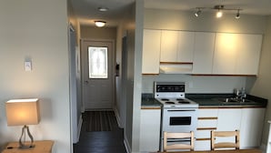 A compact kitchen with a stove, sink, and wooden cabinets. A dining table and chairs are positioned in front of the kitchen. - The Shores of Deer Lake (Unorganized Centre Parry Sound)