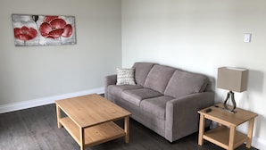 A living room with a grey sofa, a wooden coffee table, a side table with a lamp, and a painting on the wall. - The Shores of Deer Lake (Unorganized Centre Parry Sound)