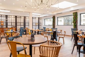 A modern dining area with multiple tables and chairs, large windows, and a decorative plant wall. - Campanile Martigny (Martigny)