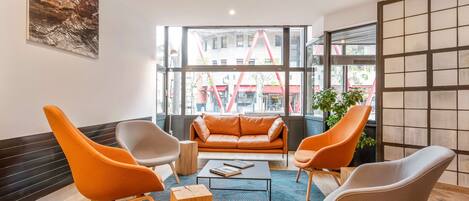A modern interior with a leather sofa, orange and grey chairs, a coffee table, and a large window with a city view.