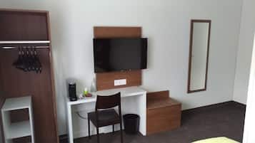 Habitación de hotel con armario de madera, escritorio con cafetera, una silla, televisor montado en la pared y un espejo.