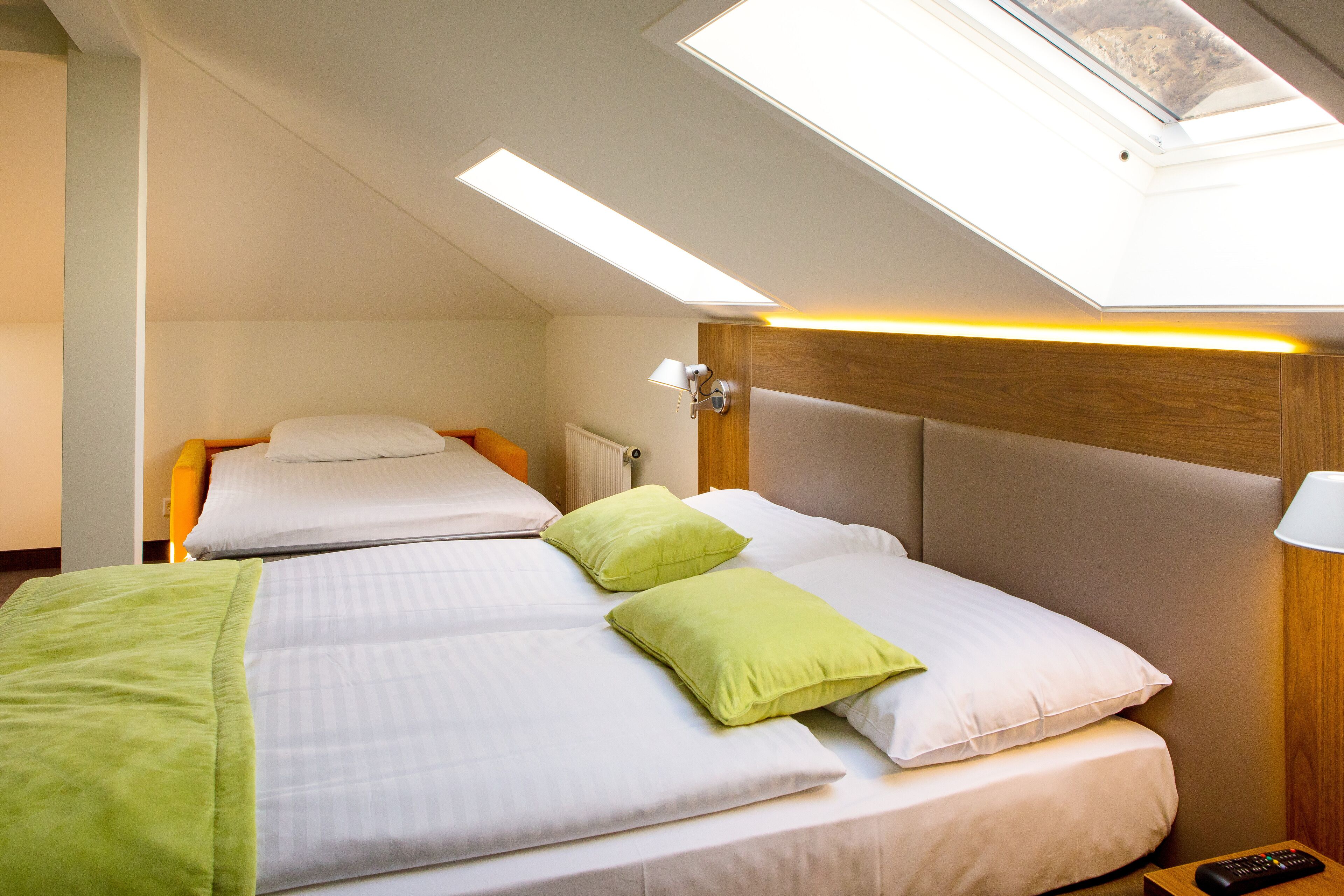 A hotel room with a skylight, two beds, a nightstand, and a remote control.